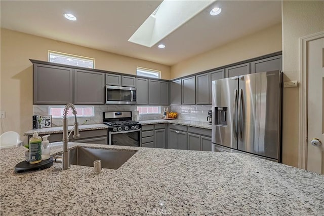 kitchen with stainless steel appliances, light stone counters, a skylight, backsplash, and sink