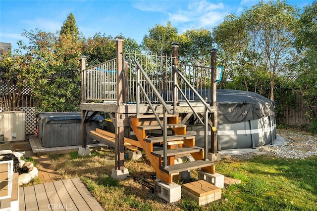 view of play area featuring a hot tub, fence, central AC unit, and a deck