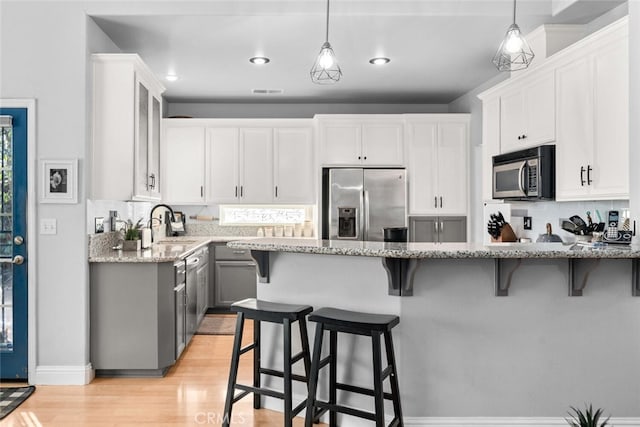 kitchen featuring stainless steel appliances, a breakfast bar area, white cabinetry, and light stone countertops