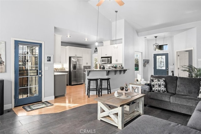 living area featuring ceiling fan, high vaulted ceiling, baseboards, and wood tiled floor