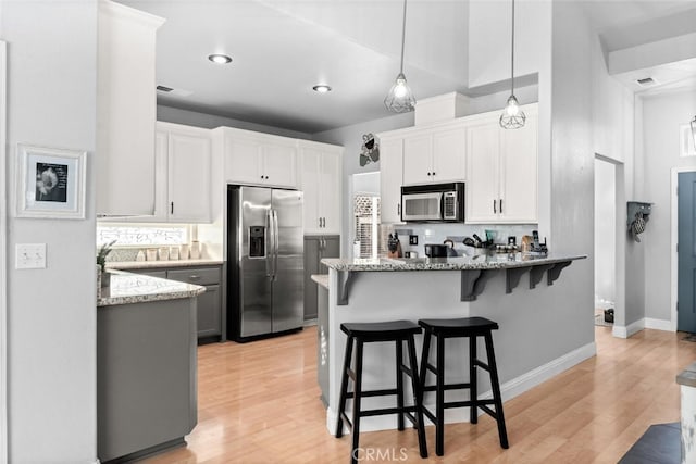 kitchen with white cabinets, a peninsula, light stone countertops, stainless steel appliances, and a kitchen bar