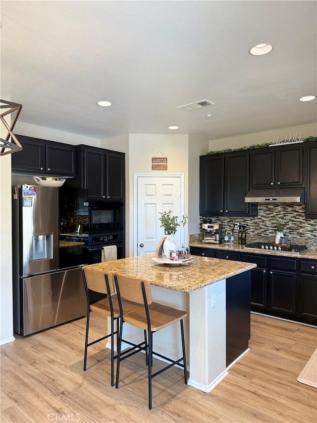 kitchen with black appliances, under cabinet range hood, visible vents, and a center island