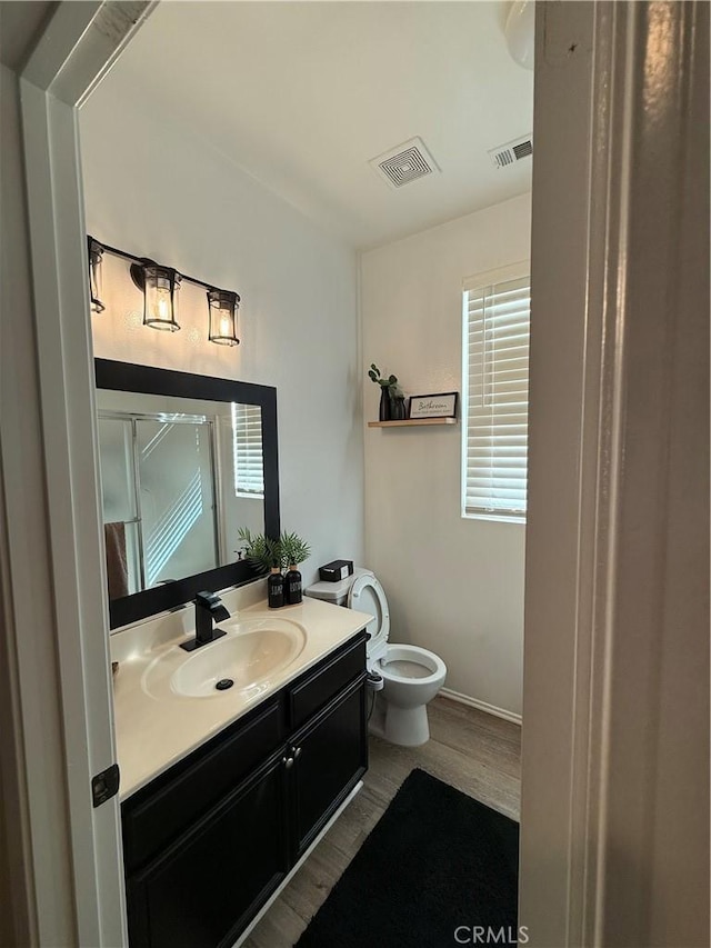 full bathroom featuring a shower with shower door, visible vents, vanity, and wood finished floors