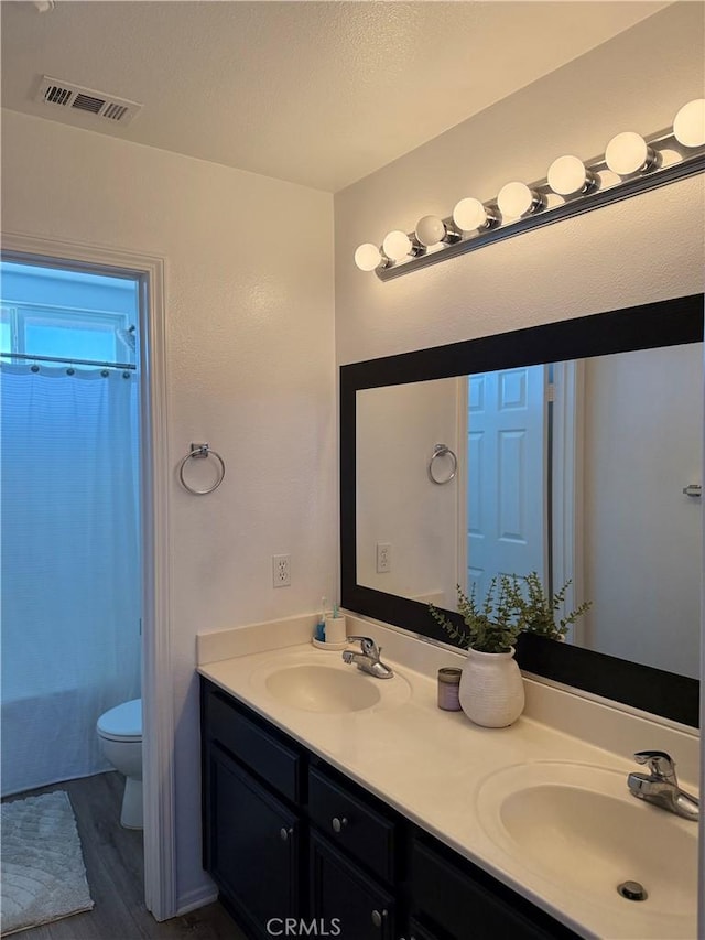 bathroom featuring toilet, double vanity, a sink, and visible vents