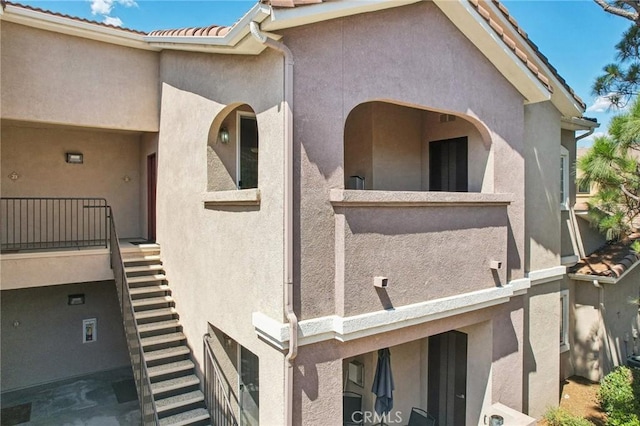 view of side of home with a balcony, a tile roof, stairs, and stucco siding