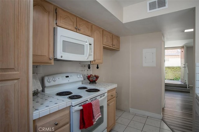 kitchen with light tile patterned flooring, white appliances, light brown cabinetry, and tile counters