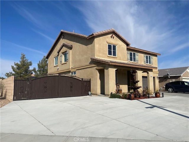 mediterranean / spanish home with stucco siding, a gate, concrete driveway, an attached garage, and a tiled roof