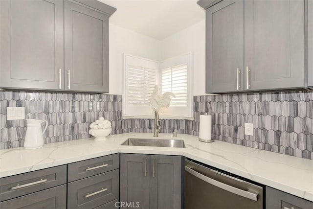 kitchen with a sink, light stone counters, gray cabinets, and dishwasher