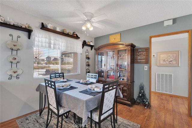 dining space with ceiling fan, wood-type flooring, and a textured ceiling