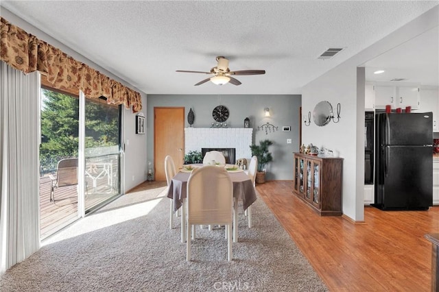 dining room with a fireplace, light hardwood / wood-style flooring, a textured ceiling, and ceiling fan