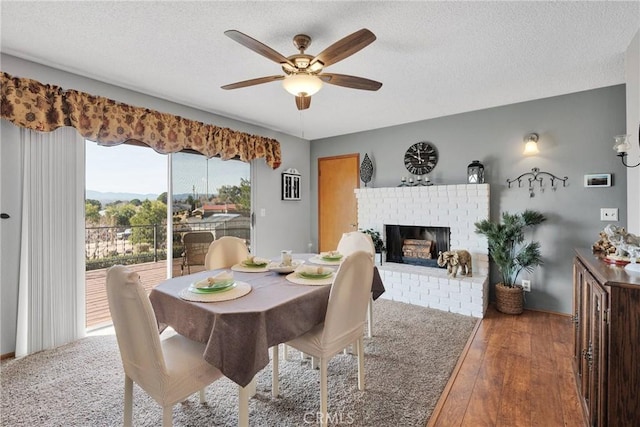 dining area with hardwood / wood-style floors, ceiling fan, a textured ceiling, and a fireplace