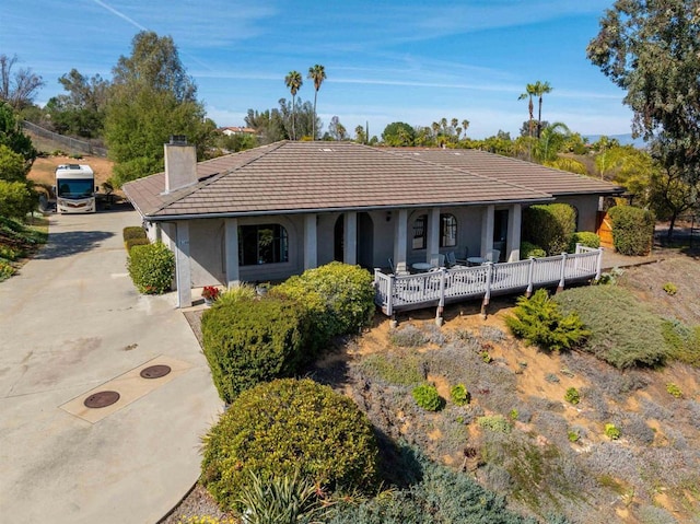 ranch-style house with a chimney, stucco siding, covered porch, concrete driveway, and a tiled roof