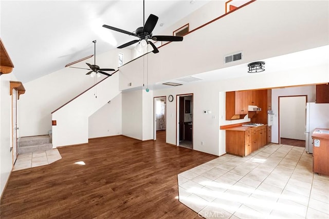 unfurnished living room featuring light wood finished floors, visible vents, a ceiling fan, stairway, and high vaulted ceiling