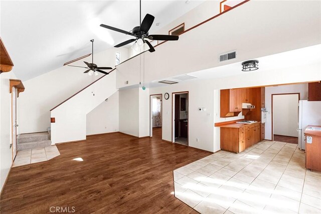 unfurnished living room featuring high vaulted ceiling, visible vents, stairway, a ceiling fan, and light wood-style floors