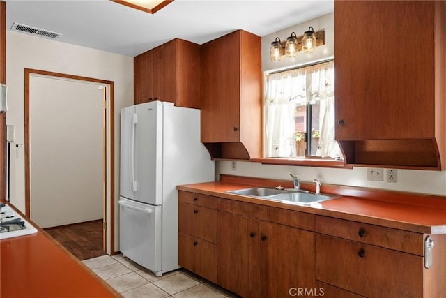 kitchen featuring white appliances, a sink, light tile patterned flooring, visible vents, and brown cabinetry