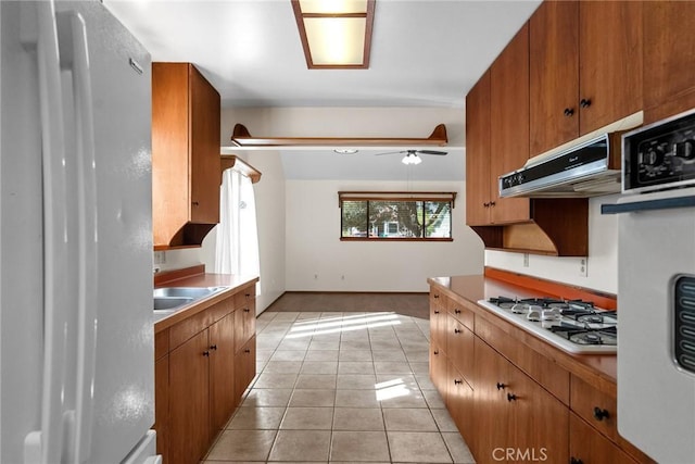 kitchen featuring white appliances, light tile patterned floors, ceiling fan, brown cabinets, and under cabinet range hood