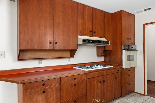 kitchen featuring white gas stovetop, under cabinet range hood, light tile patterned floors, visible vents, and oven