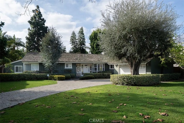 single story home with a garage, stone siding, decorative driveway, and a front yard