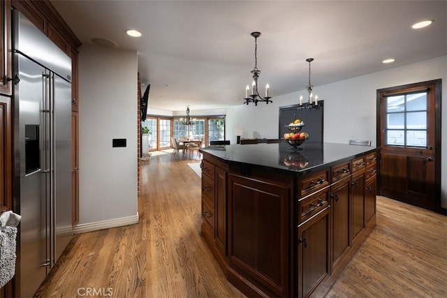 kitchen featuring dark countertops, a center island, hanging light fixtures, an inviting chandelier, and stainless steel built in refrigerator