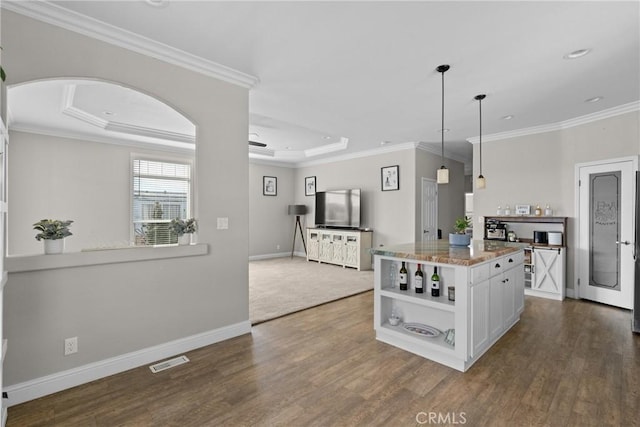 kitchen with white cabinetry, crown molding, hanging light fixtures, light stone countertops, and a raised ceiling