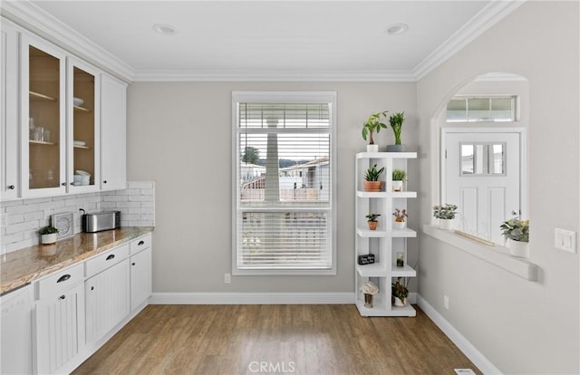 bar featuring hardwood / wood-style flooring, light stone counters, white cabinets, crown molding, and backsplash