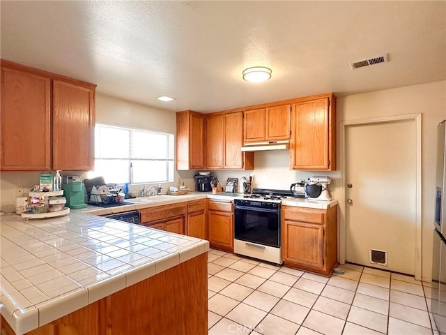 kitchen featuring light tile patterned floors, kitchen peninsula, range with gas stovetop, and tile countertops