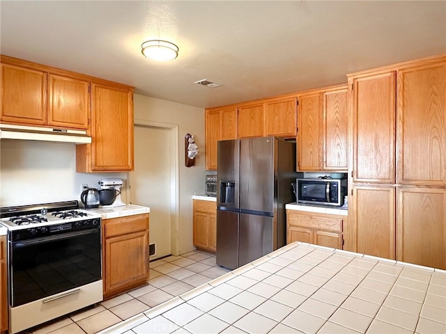 kitchen with appliances with stainless steel finishes, tile countertops, and light tile patterned floors