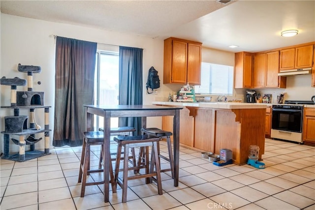 kitchen featuring light tile patterned floors, tile countertops, a breakfast bar, under cabinet range hood, and gas stove