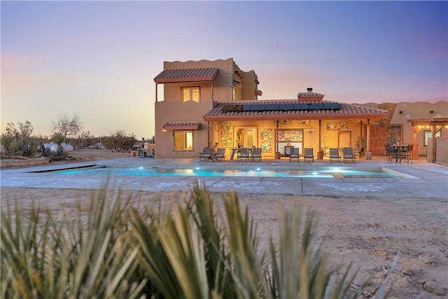 back house at dusk featuring a patio and solar panels