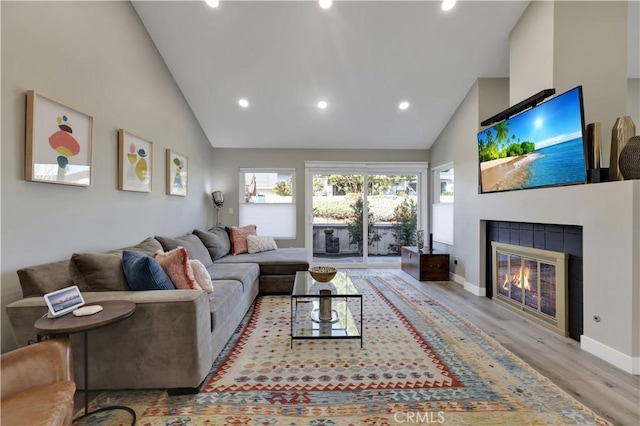 living room with high vaulted ceiling, light wood-type flooring, and a tiled fireplace