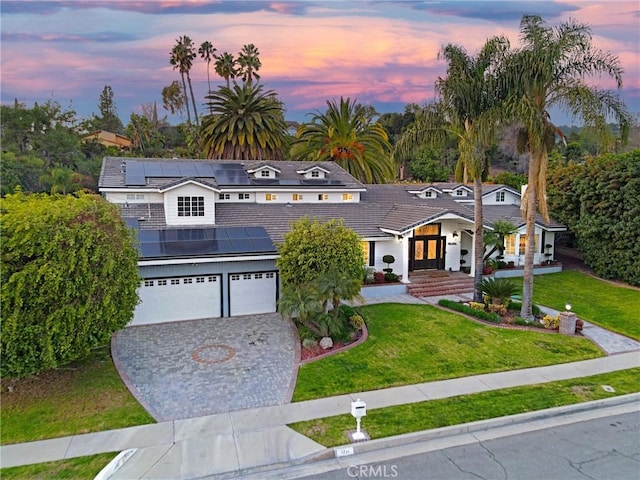 view of front of property with solar panels, a garage, and a lawn