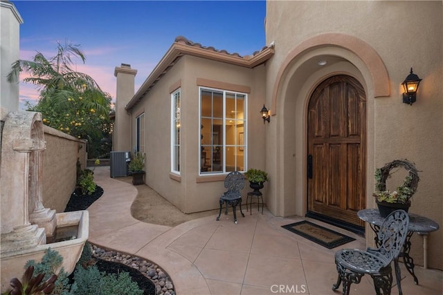 exterior entry at dusk with fence, a patio, a tiled roof, and stucco siding