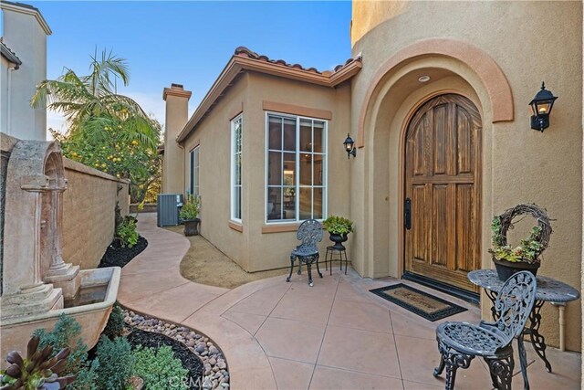 view of exterior entry featuring cooling unit, a tile roof, and stucco siding