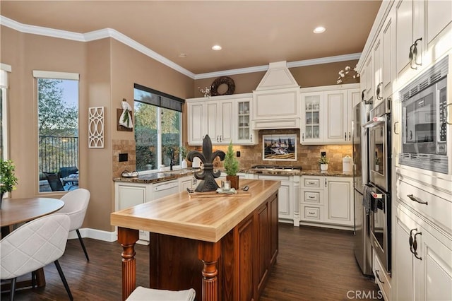 kitchen featuring butcher block countertops, crown molding, appliances with stainless steel finishes, and decorative backsplash