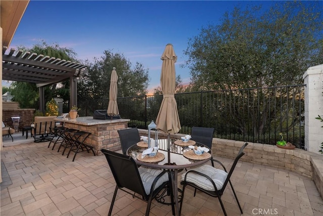 patio terrace at dusk with outdoor dry bar, area for grilling, fence, and a pergola