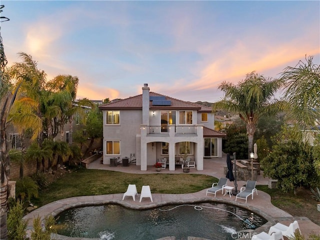 back of house featuring an outdoor pool, solar panels, a balcony, a patio area, and stucco siding