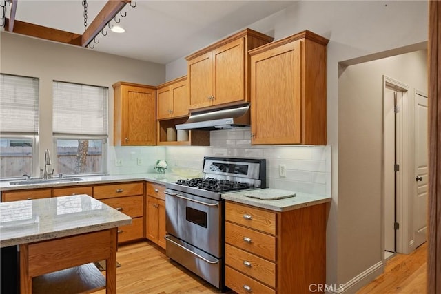 kitchen featuring a sink, light stone countertops, under cabinet range hood, stainless steel range with gas cooktop, and backsplash