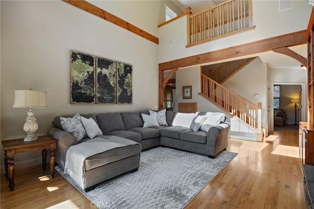 living room with light wood finished floors, visible vents, a towering ceiling, stairway, and baseboards