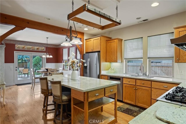 kitchen with stainless steel appliances, a sink, visible vents, light stone countertops, and decorative light fixtures