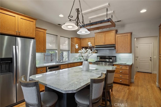 kitchen featuring a center island, hanging light fixtures, appliances with stainless steel finishes, a sink, and under cabinet range hood