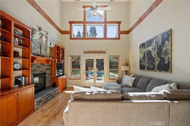 living room with light wood finished floors, a towering ceiling, ceiling fan, french doors, and a fireplace