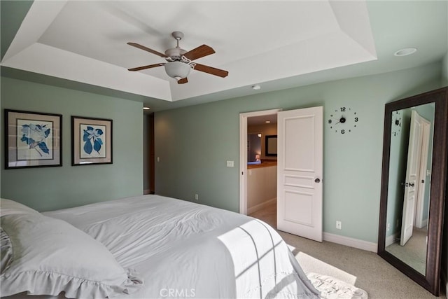 bedroom with a ceiling fan, a tray ceiling, light carpet, and baseboards