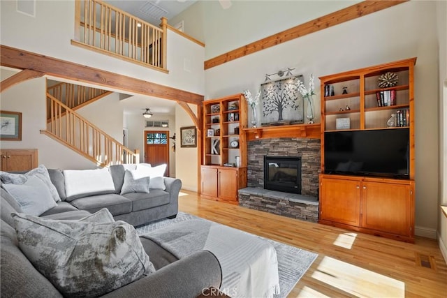 living room featuring visible vents, a towering ceiling, wood finished floors, stairs, and a stone fireplace