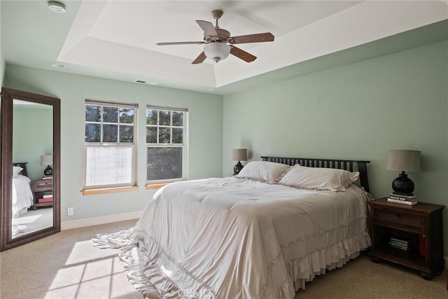 bedroom featuring ceiling fan, light colored carpet, visible vents, baseboards, and a raised ceiling