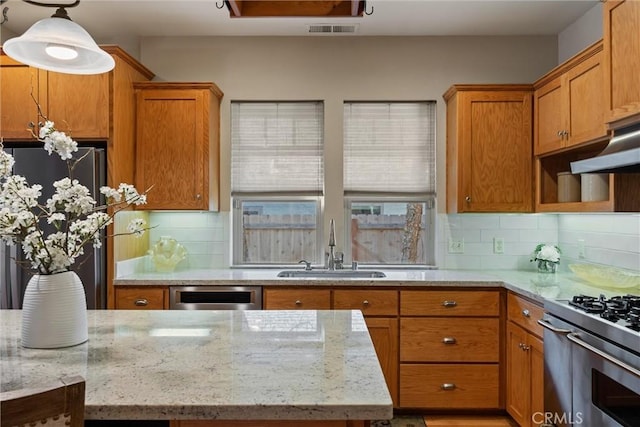 kitchen with visible vents, appliances with stainless steel finishes, decorative light fixtures, light stone countertops, and a sink