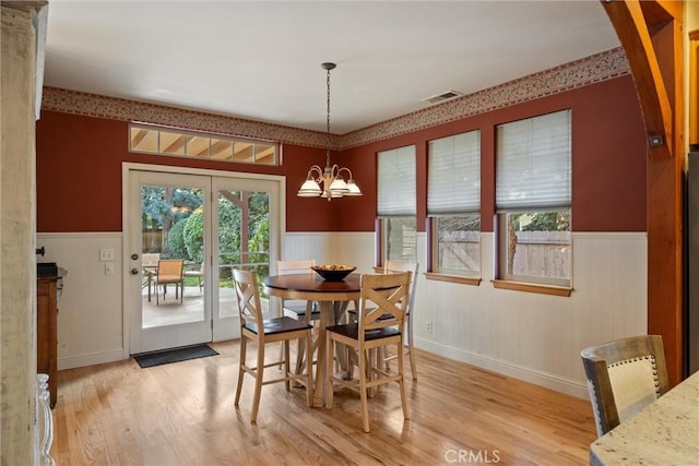 dining room featuring light wood-type flooring, a wainscoted wall, visible vents, and an inviting chandelier