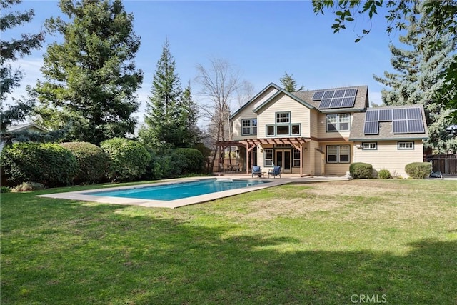 back of house with an outdoor pool, a patio, a yard, roof mounted solar panels, and a pergola