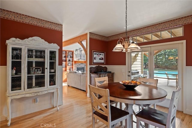 dining area with a wainscoted wall, a fireplace, an inviting chandelier, and light wood-style floors