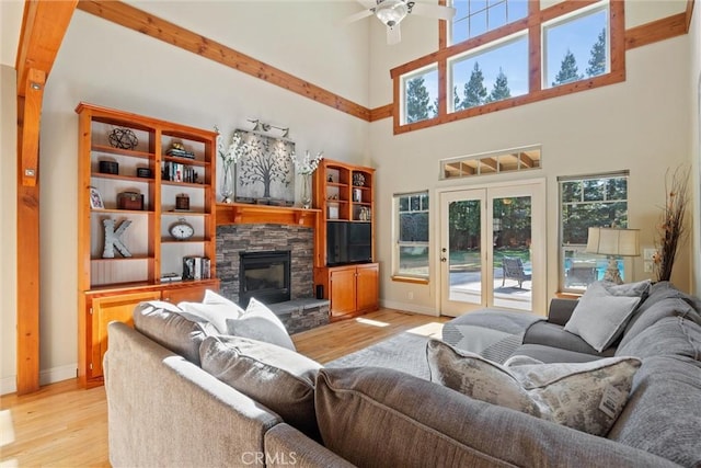 living room featuring ceiling fan, a fireplace, baseboards, and light wood-style floors