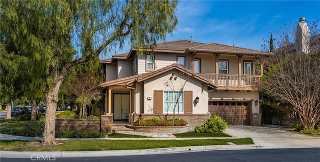 view of front of house featuring stucco siding, driveway, a balcony, an attached garage, and brick siding